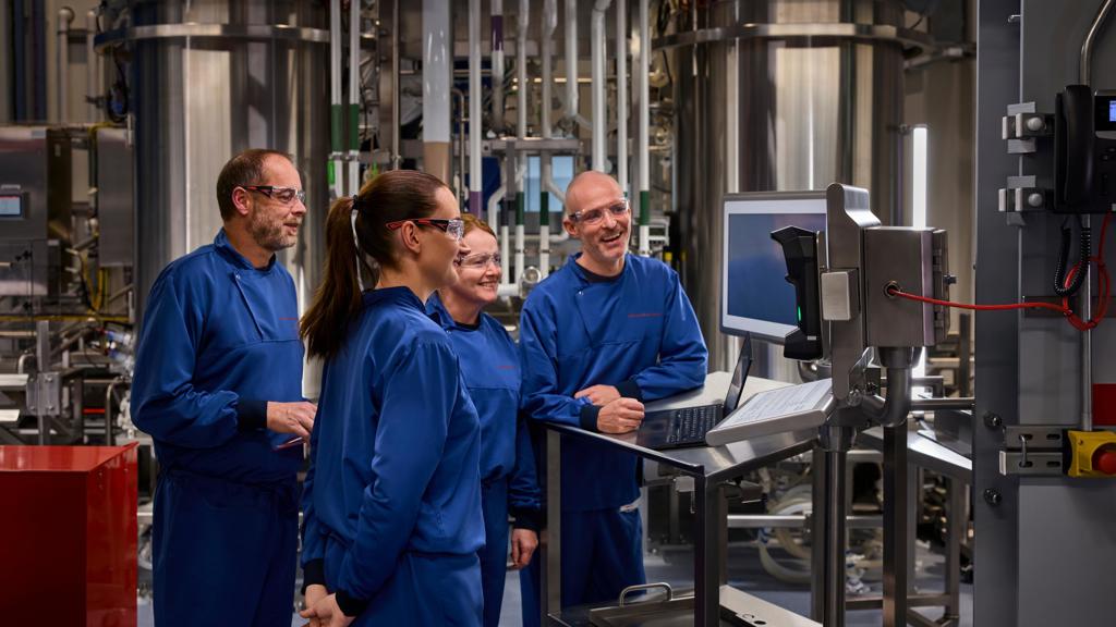 Teams collaborating at a J&J manufacturing plant wearing blue work clothes