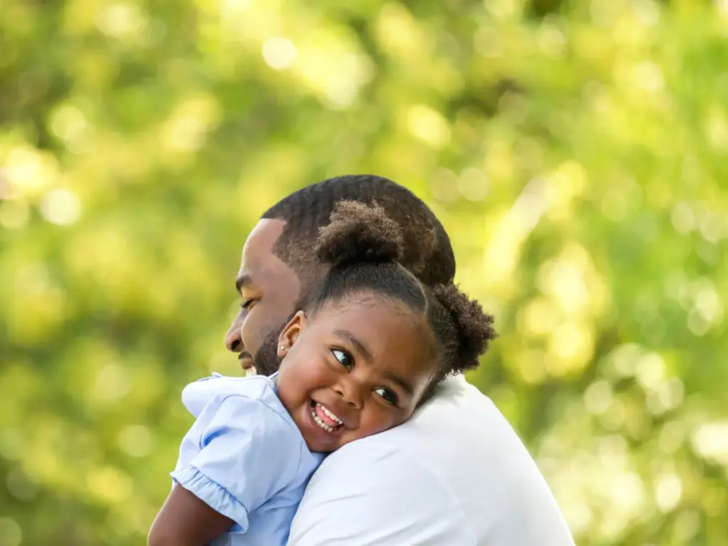 A black man holds his young daughter outside
