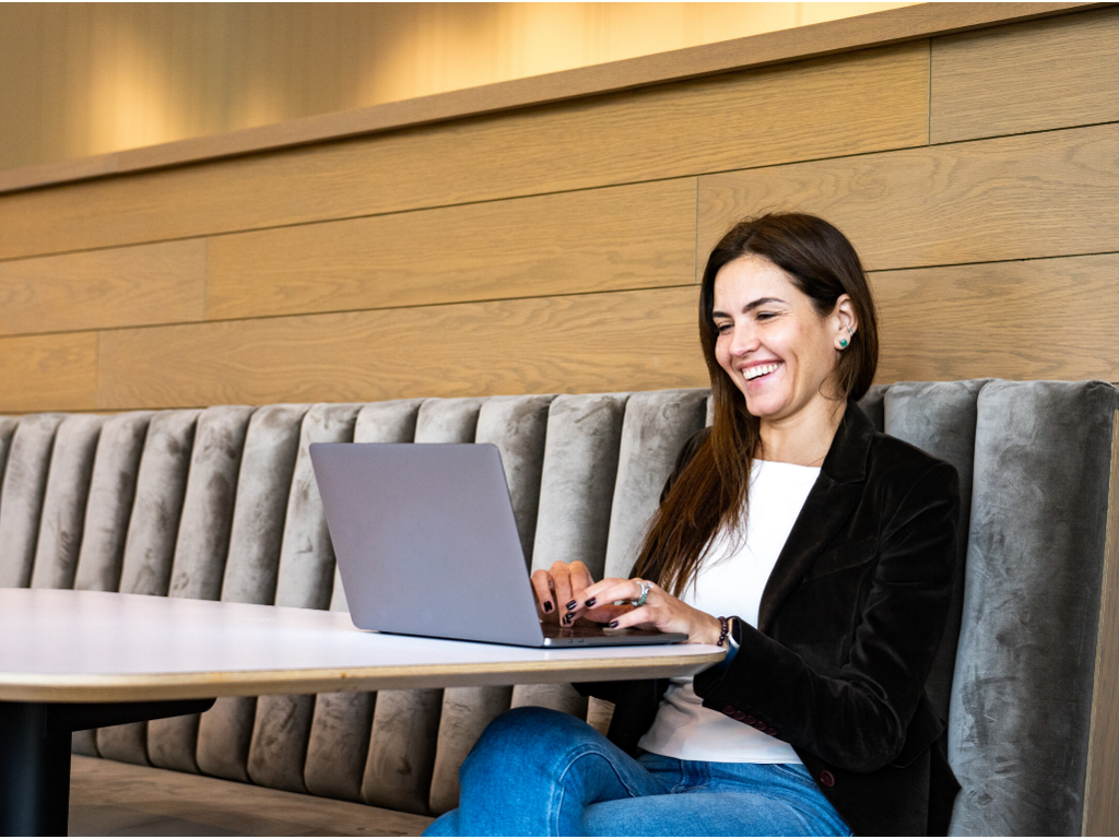 Woman sitting on a long bench working on a laptop on a table in front of her