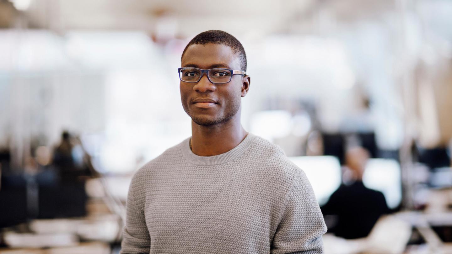 Portrait of man with glasses and grey sweater in an office setting.