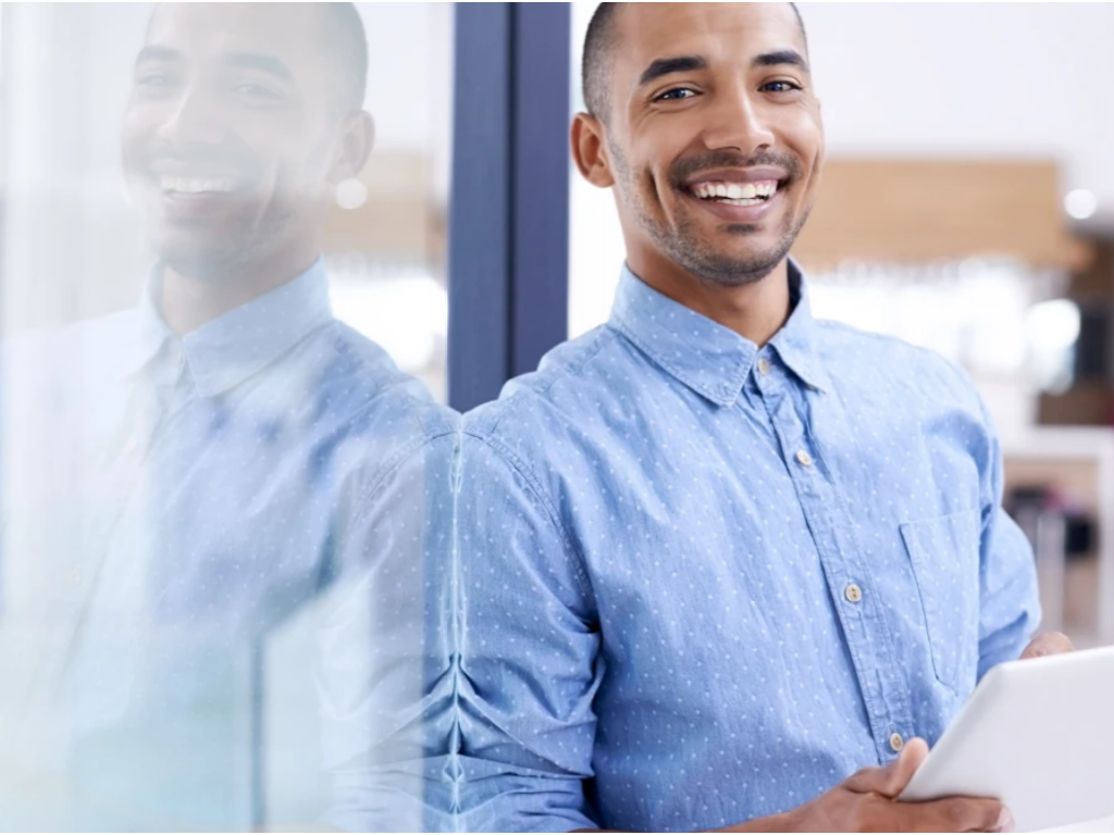 A young black man stands in front of a glass wall inside an office