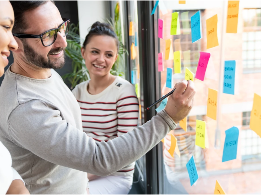 People stand in front of a glass wall covered in sticky notes planning