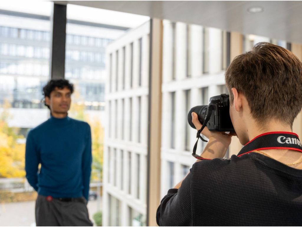 Young person holding a camera and taking a picture of someone standing against a window