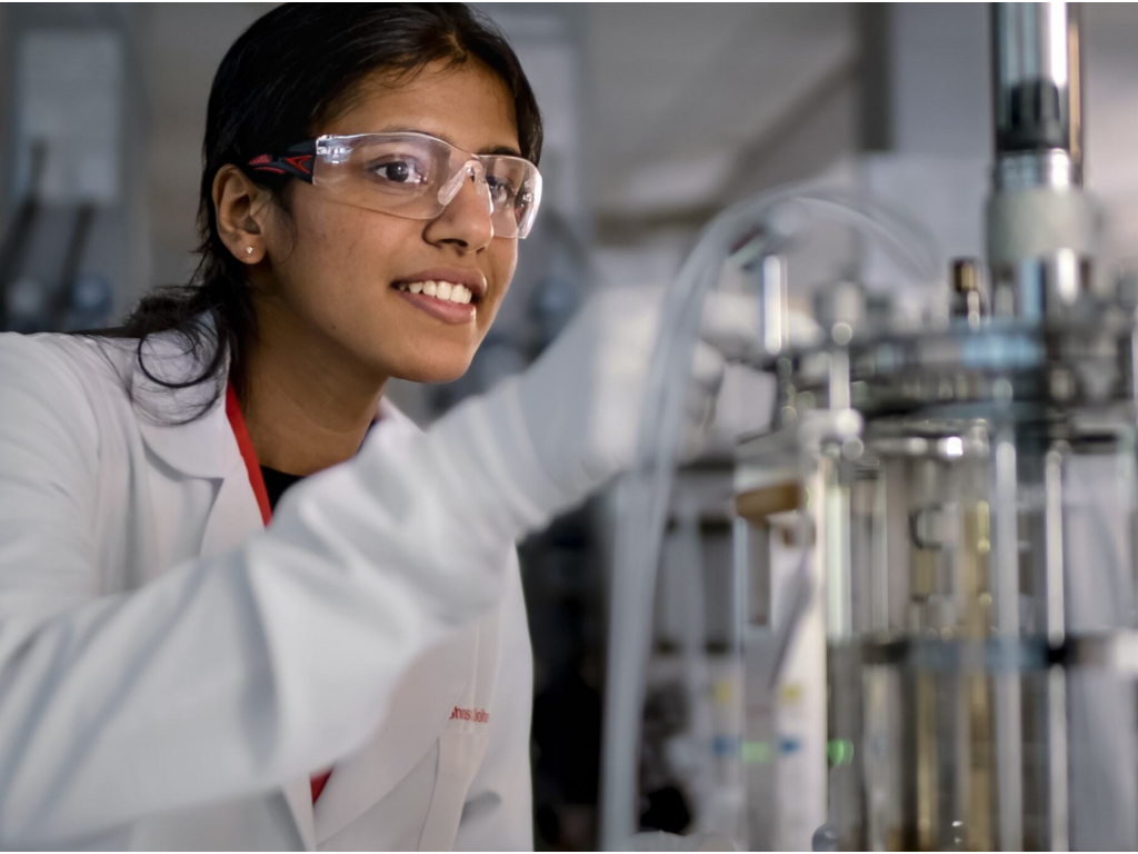 A young Black woman wearing safety goggles works in a lab with equipment