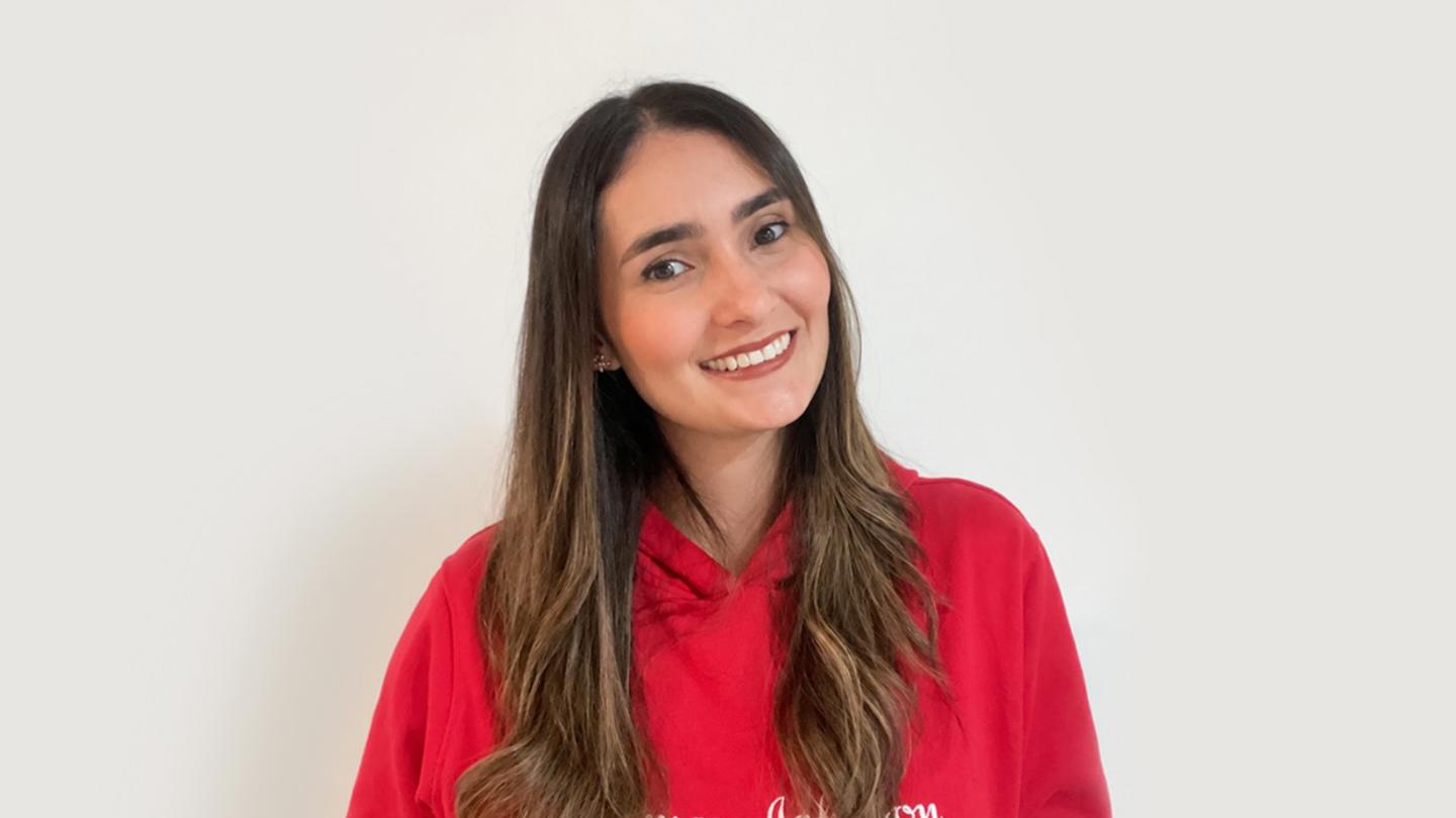 Nat, a J&J employee wearing a red sweatshirt and smiling at work.