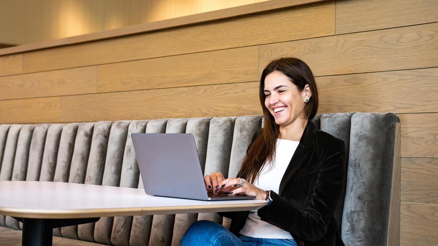 Side view of colleague participating in virtual meeting sitting in casual area of office.